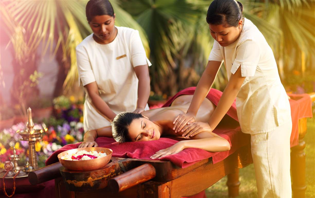Mujer soltera recibiendo un masaje de dos masajistas en un retiro de lujo en Bali.
