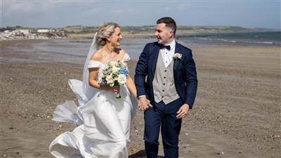 Newlyweds walking hand in hand along Garryvoe Beach