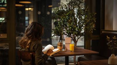 A woman reading at a table with a glass of juice at Blooms Coffee and Pizza