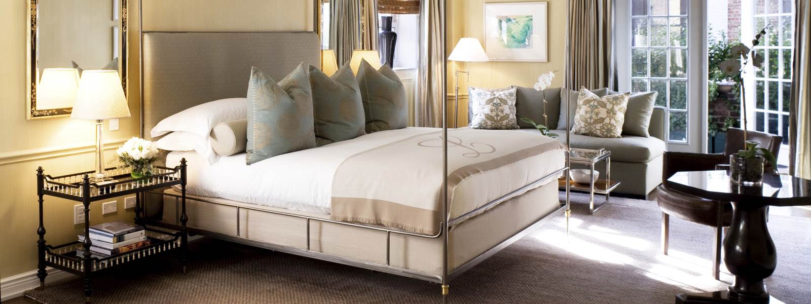A luxurious hotel room with a large bed, sofa, and table in front of a window.