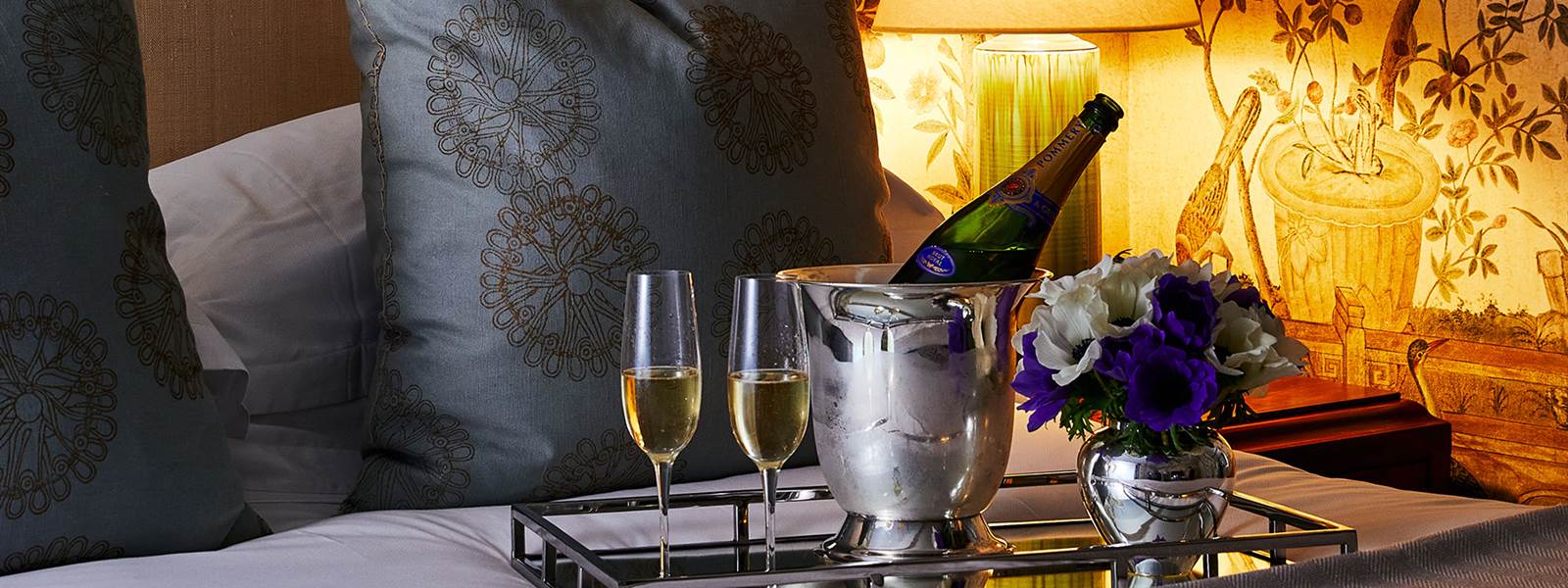 a close-up of a bed with champagne and flowers on a tray