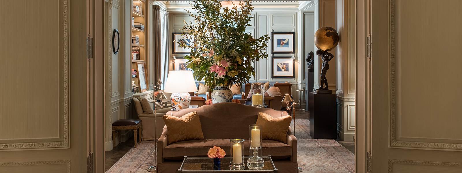 A luxurious lobby with a brown sofa, coffee table with candles and flowers, and bookshelves in the background.